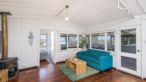 A spacious living room with a large window, a blue sofa, a wooden coffee table, and a wood-burning stove. - Love You Moore-Breathtaking Views of Both Ocean and River. (Guilderton)
