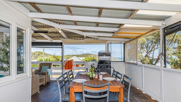 A covered outdoor dining area with a wooden table and chairs, a grill, and a view of the surrounding landscape. - Love You Moore-Breathtaking Views of Both Ocean and River. (Guilderton)