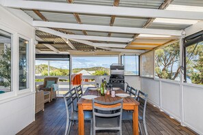 A covered outdoor dining area with a wooden table and chairs, a grill, and a view of the surrounding landscape. - Love You Moore-Breathtaking Views of Both Ocean and River. (Guilderton)