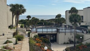 A resort with a pool, palm trees, and a view of the ocean. - Dove's Island Nest - Cozy Condo, Pool, Near Beach, Tennis Courts, Ocean Views (St. Augustine)