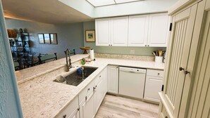 A kitchen with white cabinets, a dishwasher, a sink with a faucet, and a skylight above. - Dove's Island Nest - Cozy Condo, Pool, Near Beach, Tennis Courts, Ocean Views (St. Augustine)