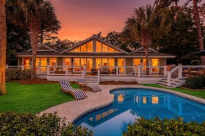 Uma casa grande com piscina, alpendre coberto e gramado bem cuidado.