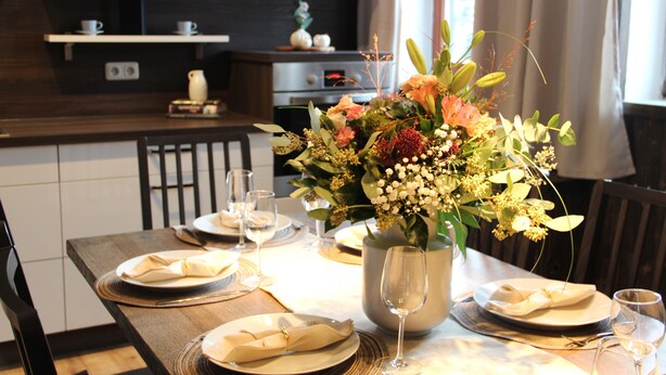 A dining table set with plates, glasses, and a centerpiece of flowers. - Vacation in a half-timbered house, experience a real piece of living history. (Sehmatal-Neudorf)