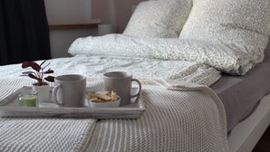 A neatly made bed with a white blanket and pillows, a tray with two mugs, a small bowl of cookies, and a potted plant. - Vacation in a half-timbered house, experience a real piece of living history. (Sehmatal-Neudorf)