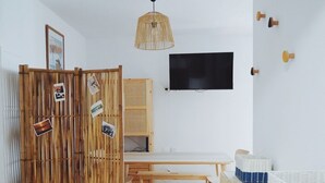 Ein Zimmer mit Holzboden, einem Esstisch mit Bänken, einem an der Wand montierten Fernseher und einer Korblampe.