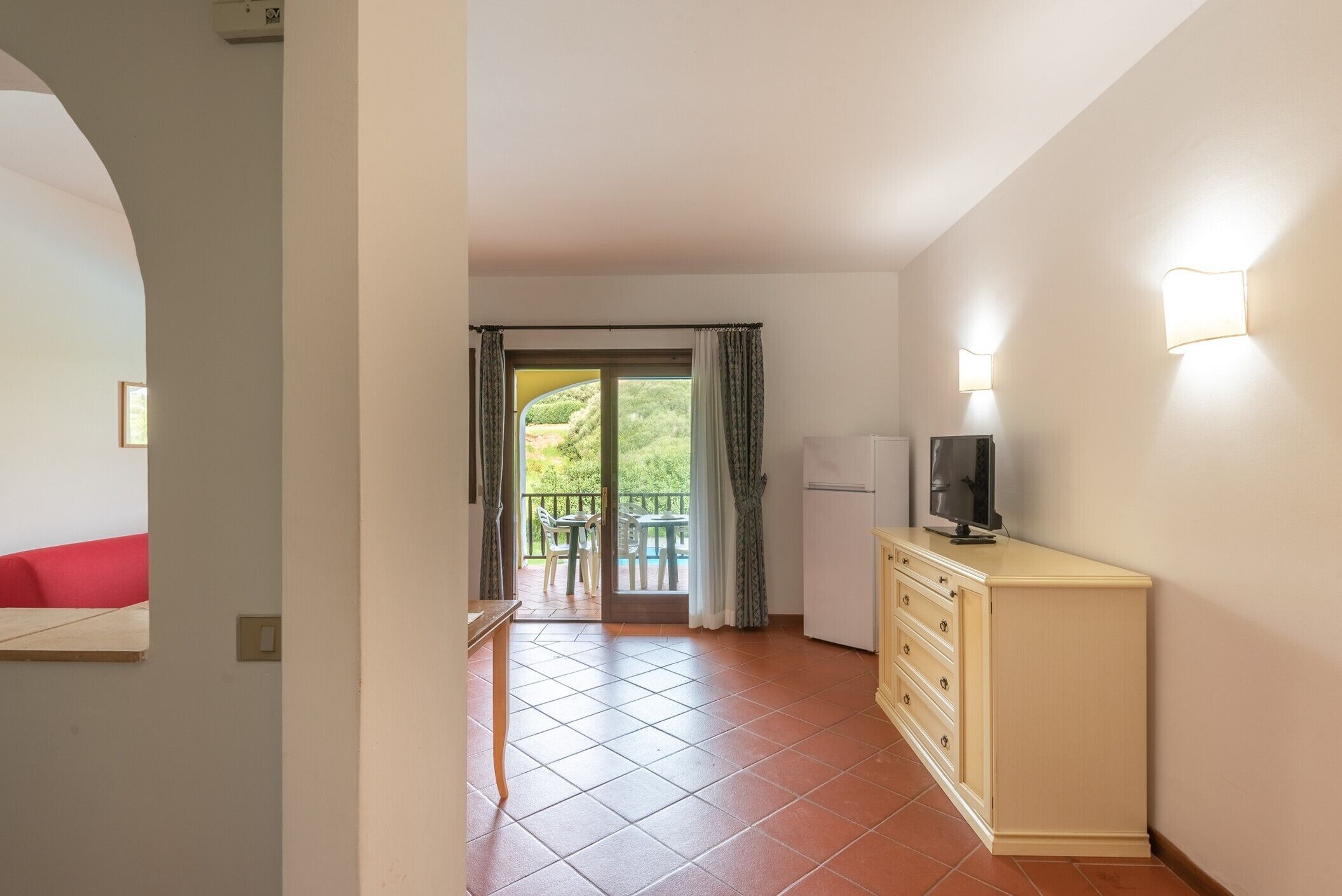 En kompakt opholdsstue med tekøkken, et fladskærms-tv og en balkon med et bord og stole.