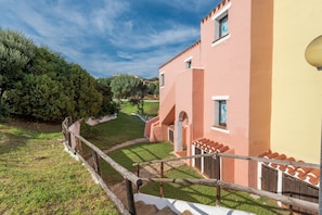 Un bâtiment à la façade rose, une clôture en bois et un espace verdoyant avec des arbres.