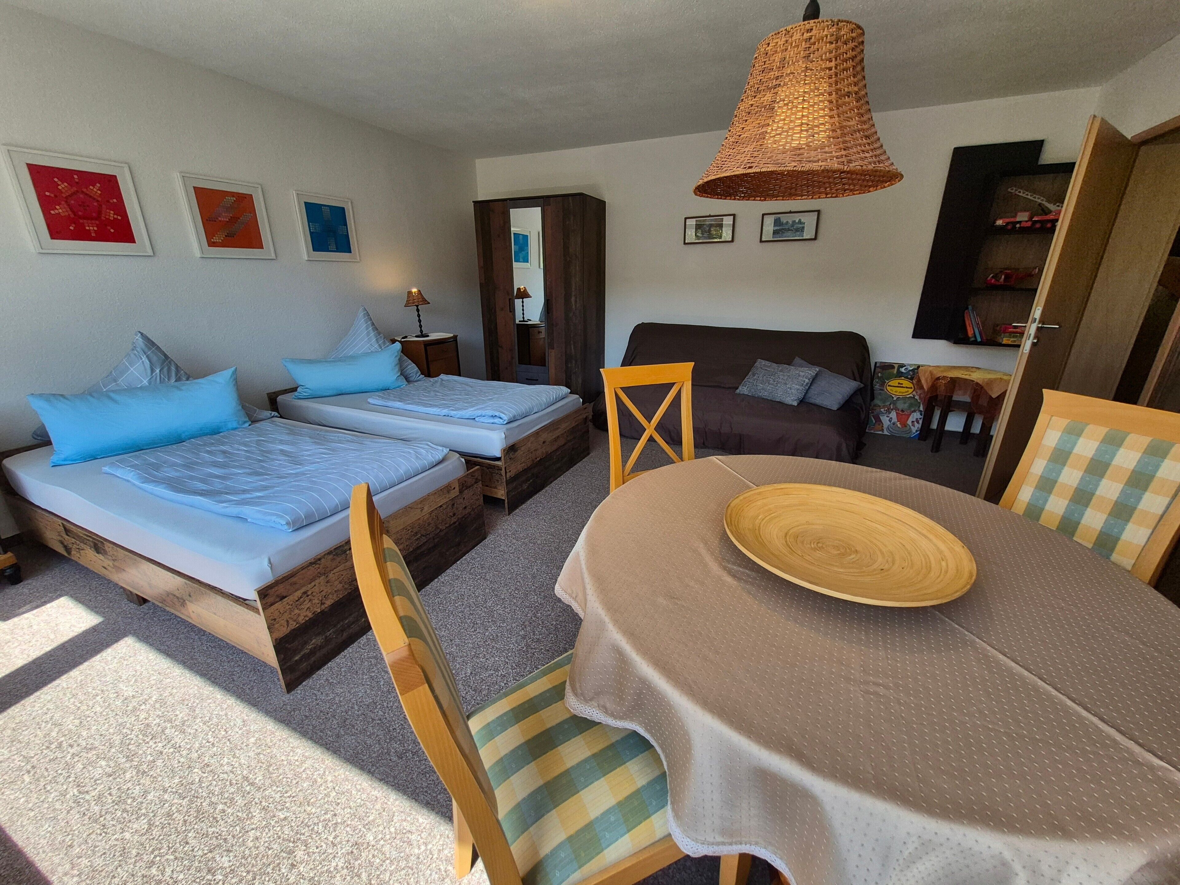 Une chambre avec deux lits, un canapé, une table à manger avec un set de table et une lampe suspendue.