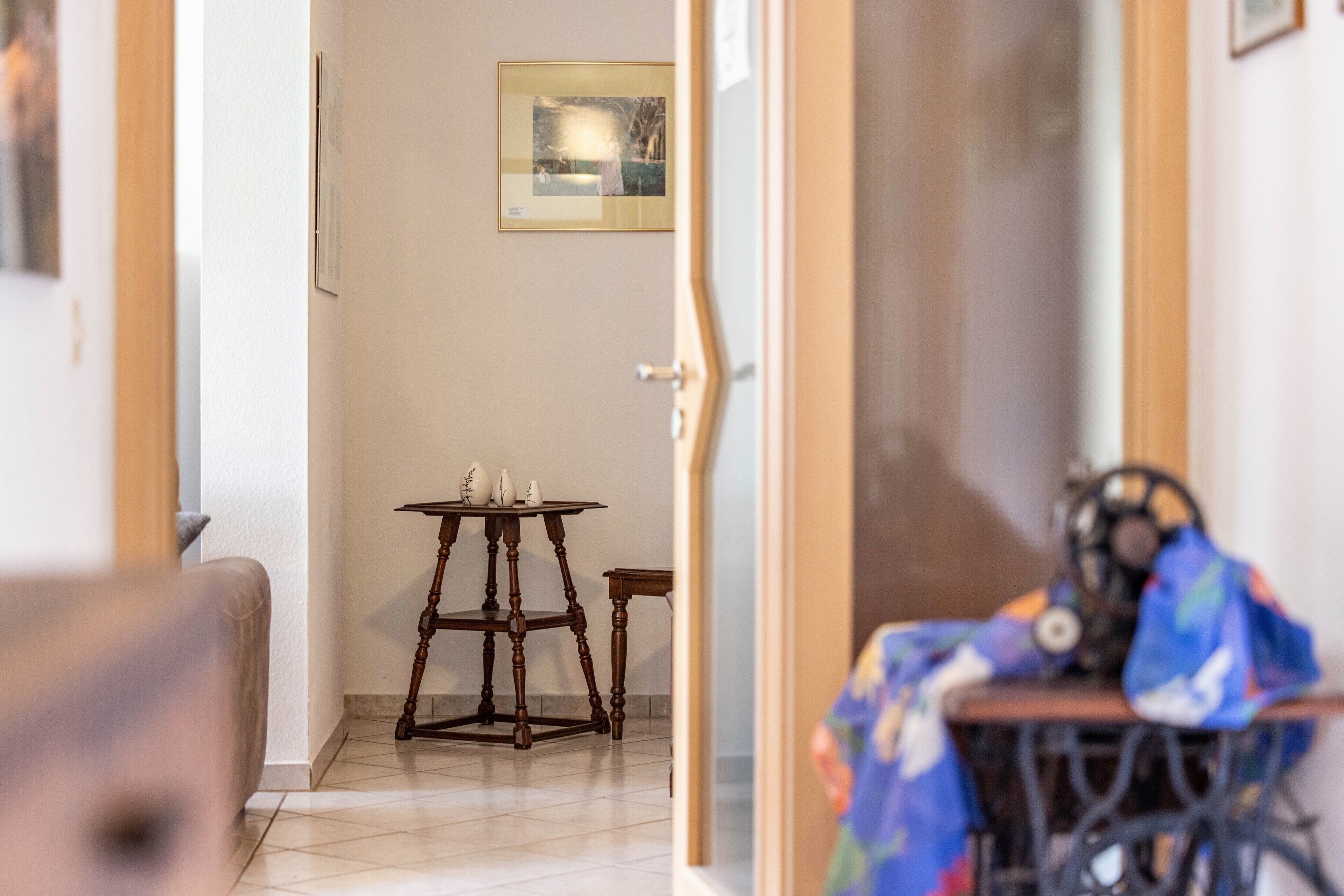 Une pièce comprenant une machine à coudre, une petite table ornée d’objets décoratifs et un tableau encadré accroché au mur.
