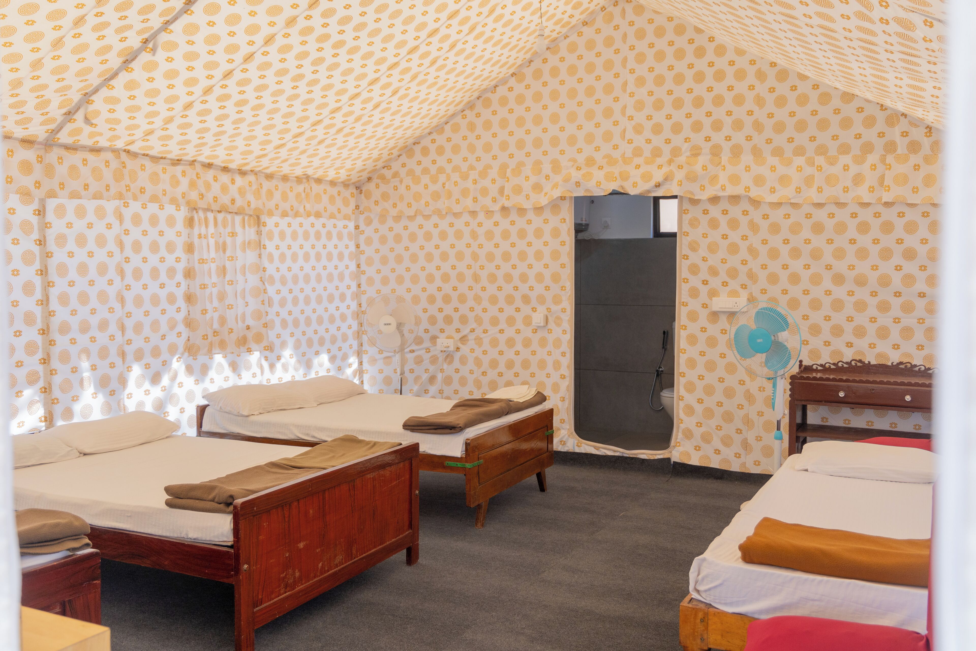 Ein Zimmer mit zwei Betten, einer Holzbank, einem kleinen Tisch und einem Ventilator.