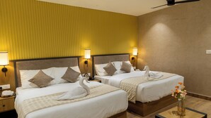 Ein Hotelzimmer mit zwei Betten, Holzboden, Deckenventilator und einer Vase mit Blumen auf einem kleinen Tisch.