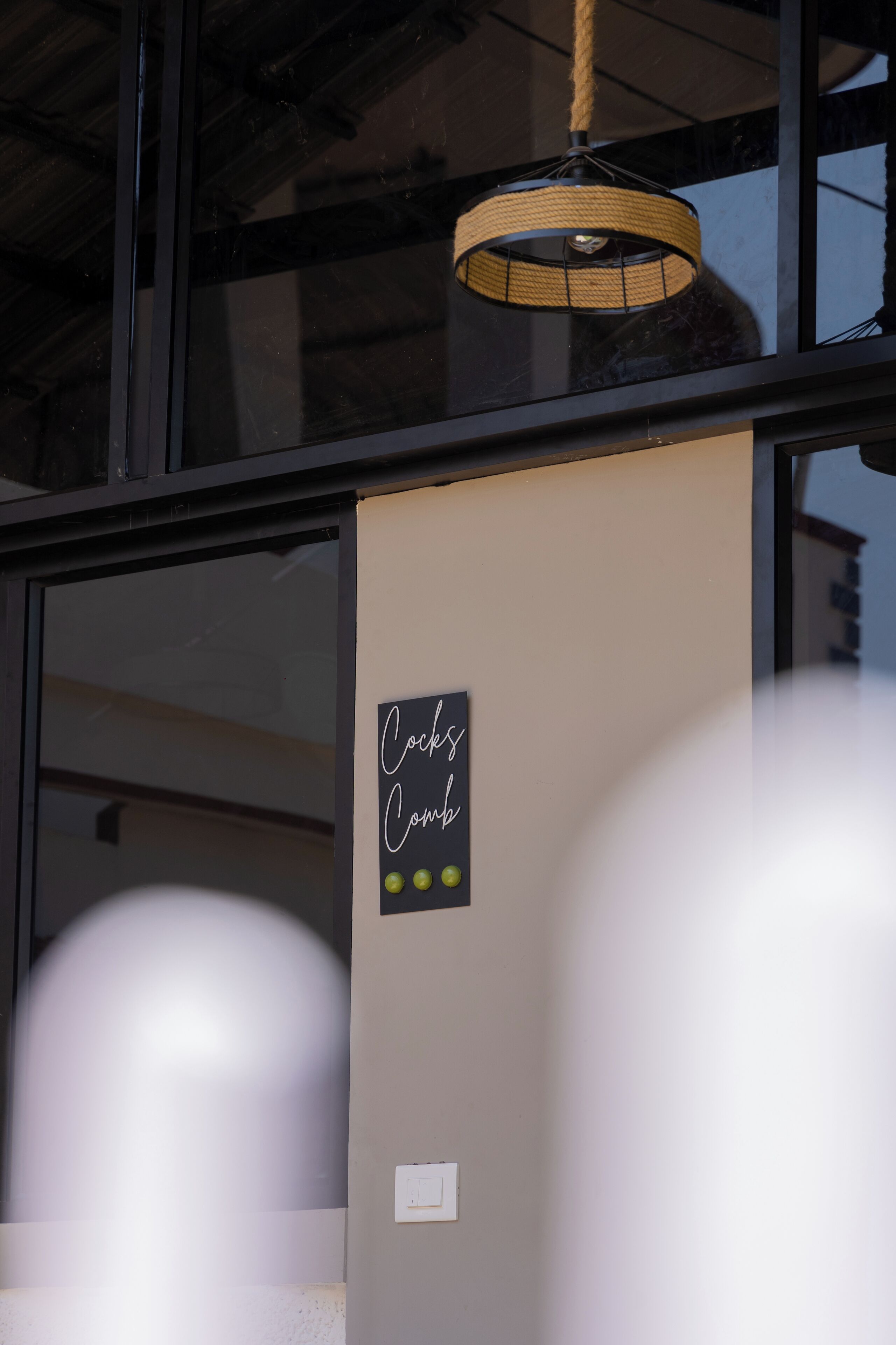 A sign on a wall that reads "Cocks Comb" with a light fixture above it.