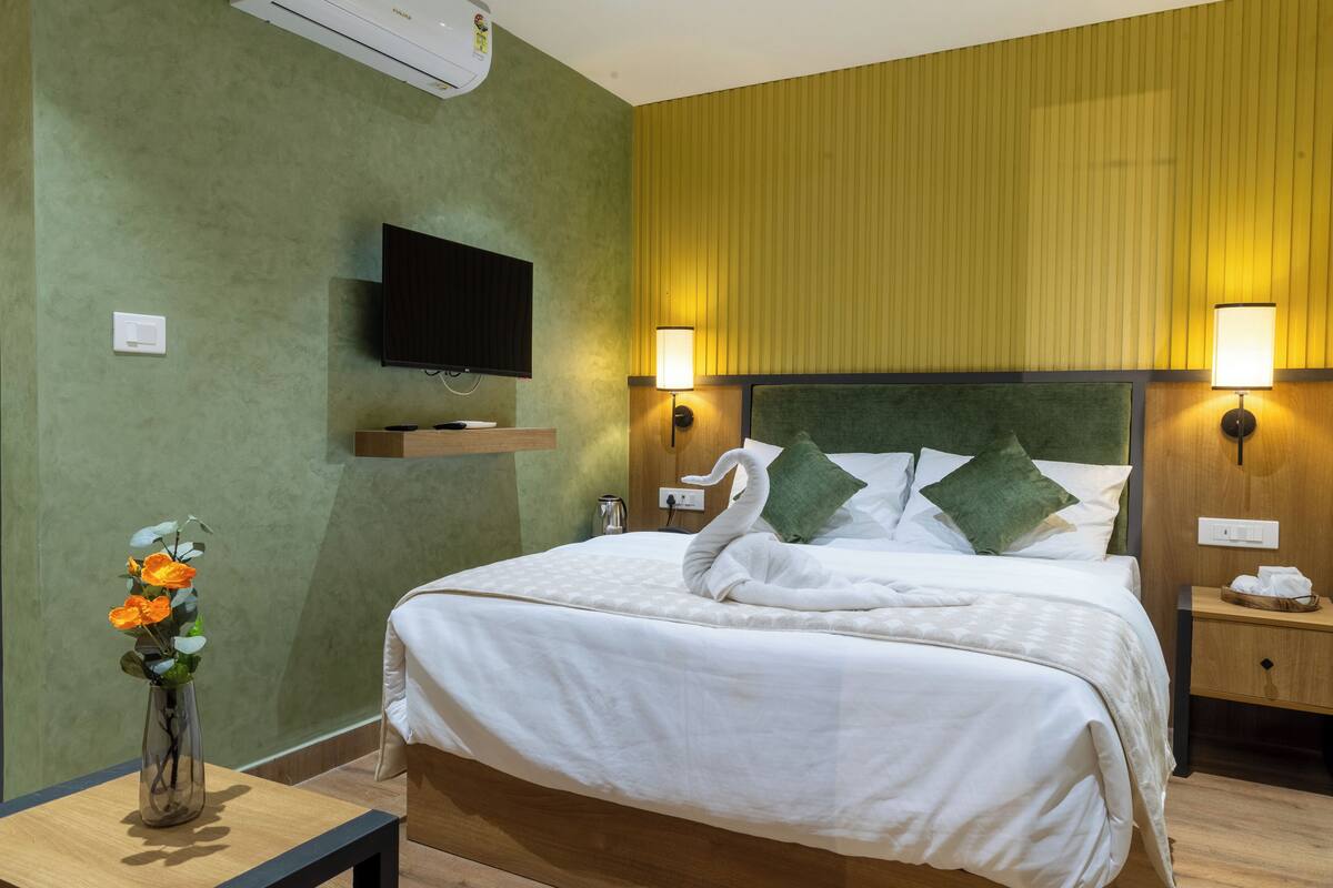A neatly made bed with a swan-shaped pillow, a bedside table with a lamp, and a TV mounted on the wall.