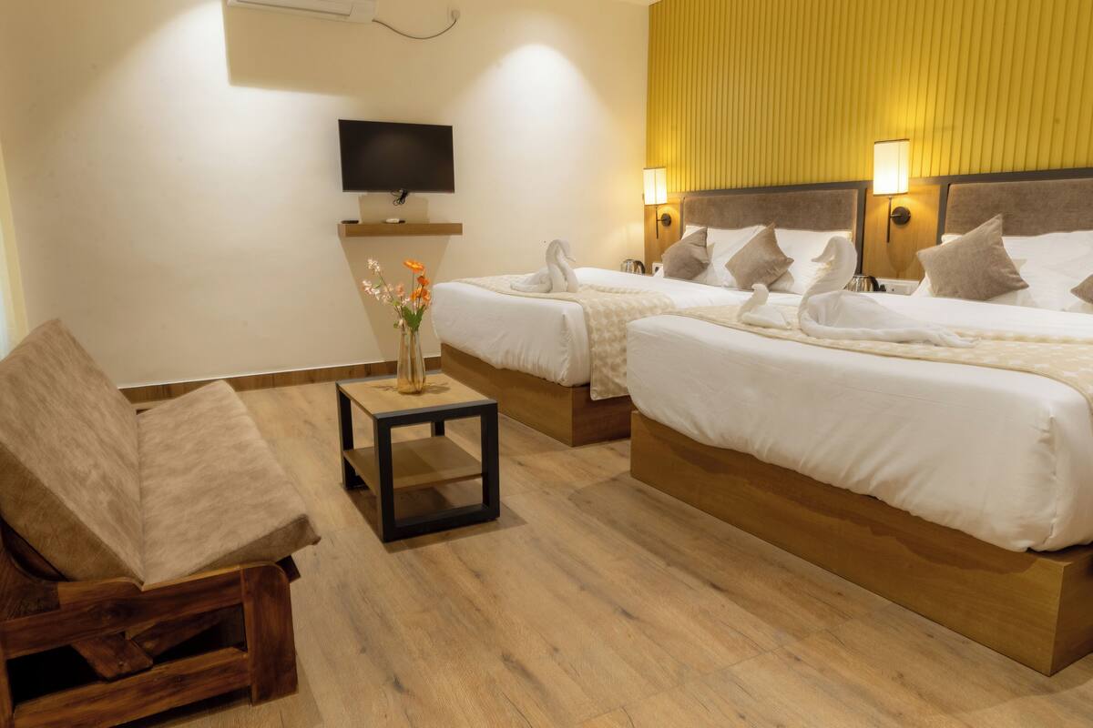 A hotel room with two beds, a TV, a small table with a vase, and a wooden chair.
