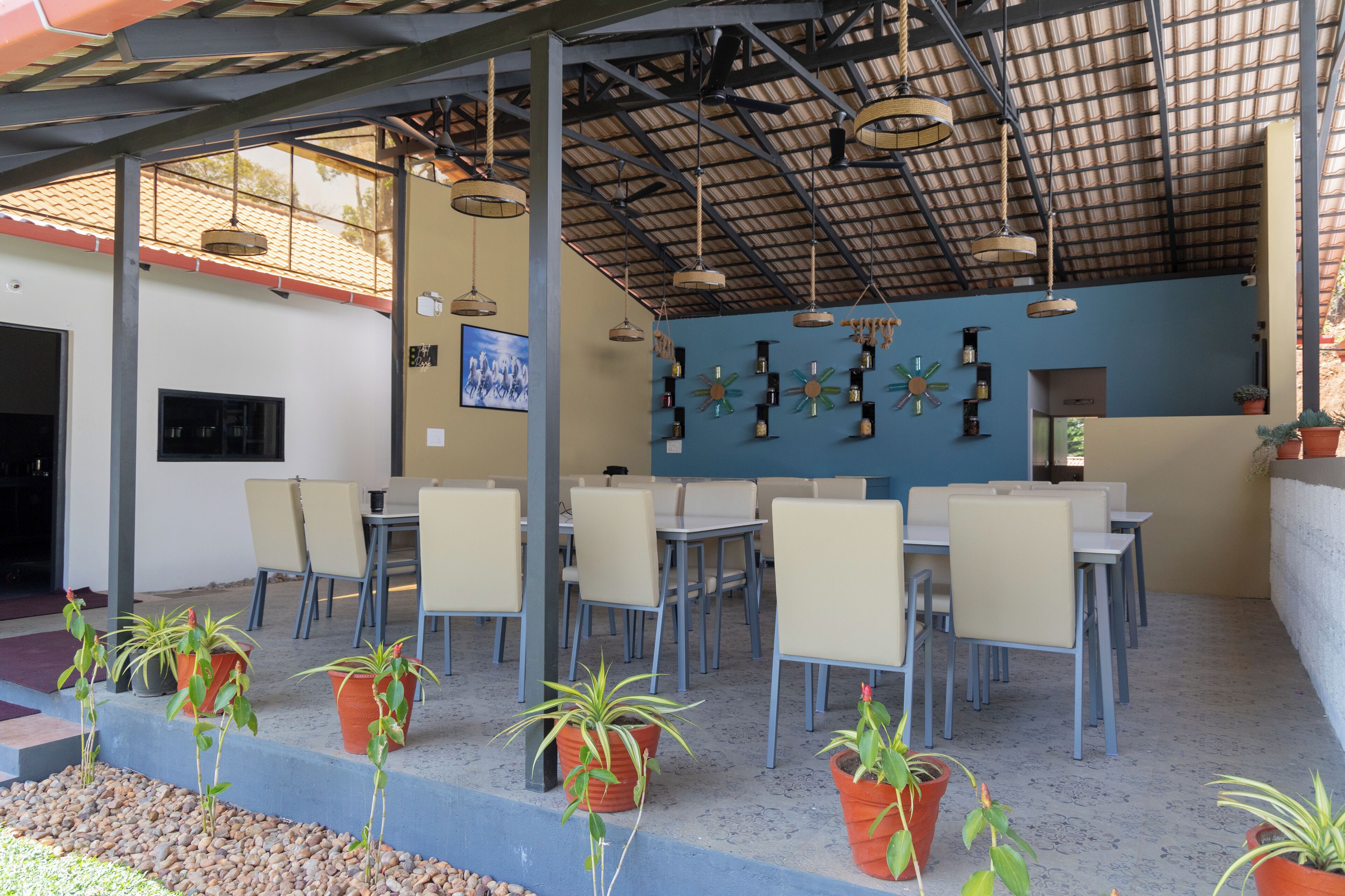 An outdoor cafe with tables and chairs, potted plants, and a blue wall with decorative items.