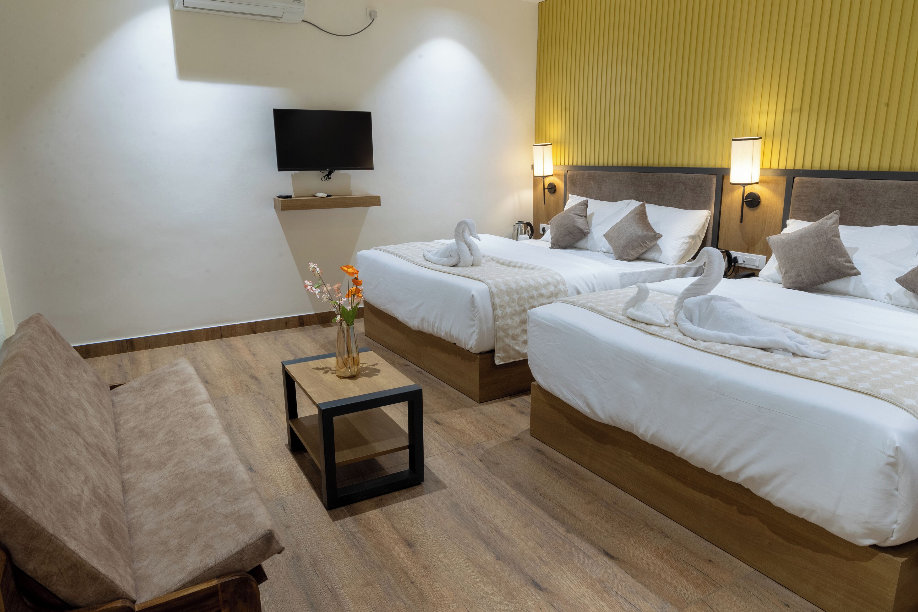 A hotel room with two beds, a TV, a small table with a vase, and a chair.