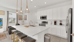A modern kitchen with white cabinets, a central island with stools, stainless steel appliances, and pendant lighting. - 3 Beds 3 Baths Cozy Town Home 3 Bedroom Townhouse (Davenport)