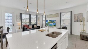 A modern kitchen with a large island, pendant lighting, and a view of the city through large windows. - 3 Beds 3 Baths Cozy Town Home 3 Bedroom Townhouse (Davenport)