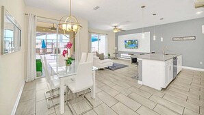 A modern kitchen with a central island, a dining area with a glass table, and a living space with a sofa and TV. - Beautiful Paradise Palms Retreat 4 Bedroom Townhouse (Kissimmee)
