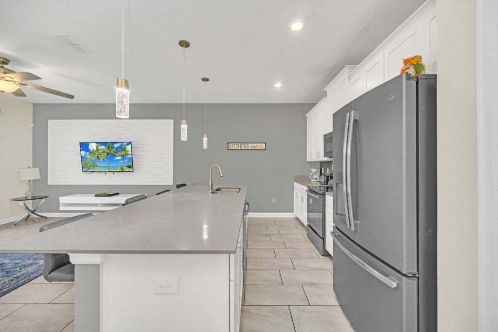 A modern kitchen with a large island, stainless steel appliances, pendant lighting, and a view of the outdoors.