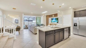 A modern kitchen with a large island, stainless steel appliances, and a dining area with a staircase. - Amazing Theme Rooms Kids Will Love! 5 Bedroom Townhouse (Clermont)