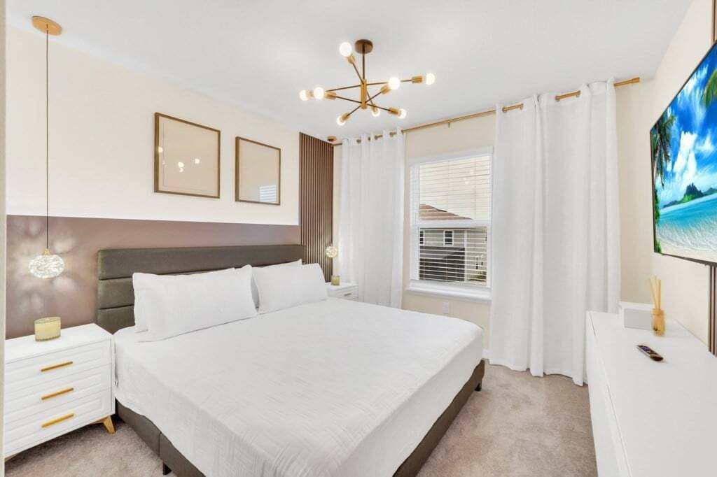 A bedroom with a large bed, a nightstand, a bedside table, a TV, and a window with curtains.
