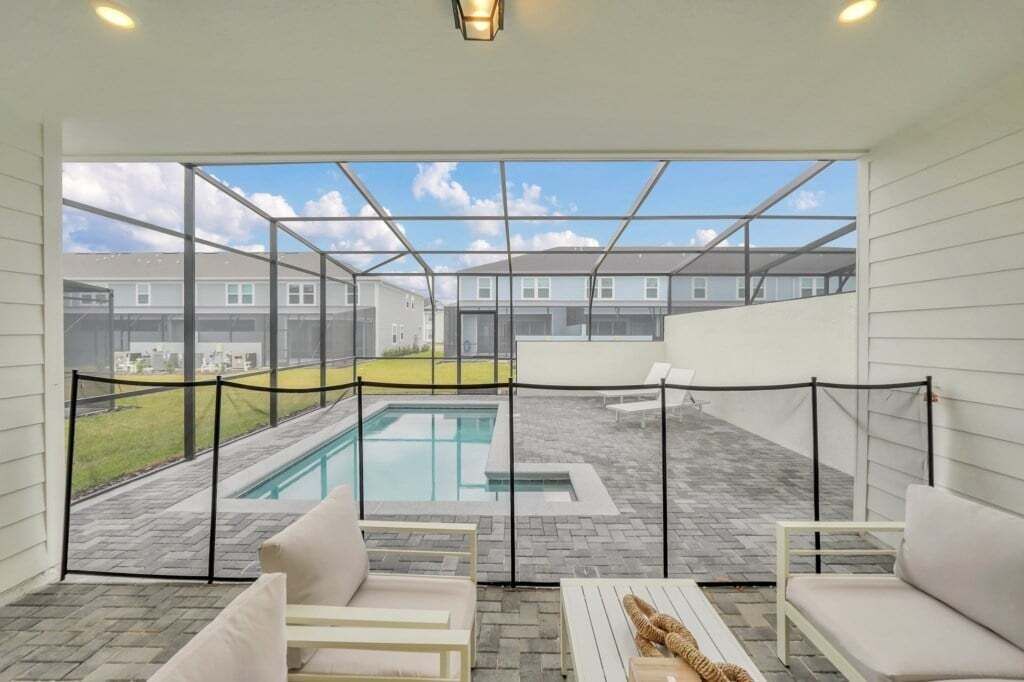 A poolside area with a view of neighboring houses, a fenced pool, and outdoor seating.