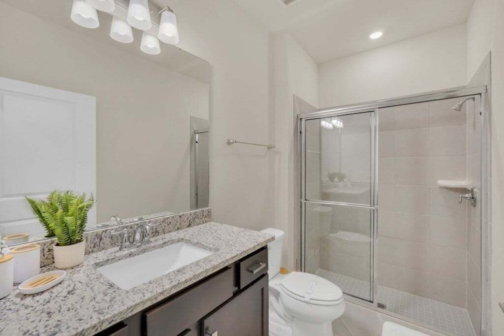 A modern bathroom with a granite countertop, a white sink, a toilet, and a glass-enclosed shower.