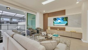 A modern living room with a large TV, comfortable seating, and a glass door leading to an outdoor area. - Amazing Theme Rooms Kids Will Love! 5 Bedroom Townhouse (Clermont)