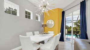 A dining area with a white table and chairs, a round mirror on the wall, and a view of a swimming pool through large windows. - 5 Bed Multiple Bunks Perfect For Kids With Pool! 5 Bedroom Townhouse (Davenport)