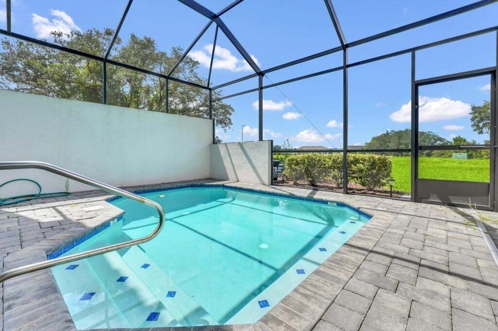 An indoor swimming pool with clear blue water, surrounded by a brick floor and a glass enclosure.