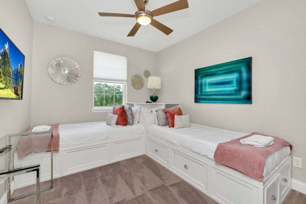 A bedroom with two beds, a ceiling fan, a window, and artwork on the walls.