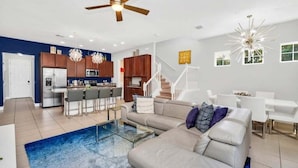 A modern living room with a sofa, coffee table, and a dining area with a white table and chairs. - 5 Bed Multiple Bunks Perfect For Kids With Pool! 5 Bedroom Townhouse (Davenport)