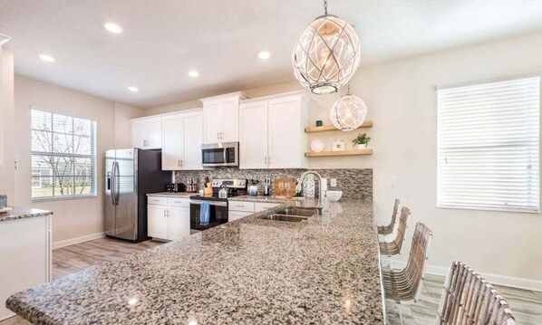 A modern kitchen with granite countertops, stainless steel appliances, and pendant lighting. - Spacious 5 Bed Pool Home With Game Room 5 Bedroom Home (Davenport)