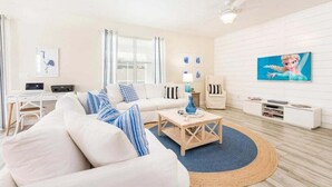 Un salon moderne avec un canapé blanc, une table basse et un téléviseur fixé à un mur blanc. On y trouve également un bureau avec un ordinateur et une lampe.