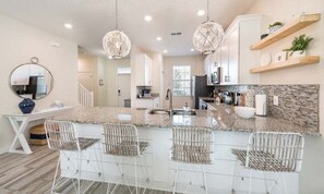 A modern kitchen with granite countertops, white bar stools, pendant lighting, and a backsplash. - Spacious 5 Bed Pool Home With Game Room 5 Bedroom Home (Davenport)