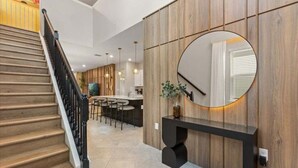 Ein modernes Interieur mit einer Holztreppe, einem runden Spiegel und einer Essecke mit Barhocker.