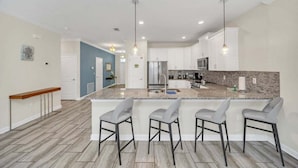 A modern kitchen with a central island, bar stools, and pendant lighting. - Modern Beautiful Private Pool Home! 9 Bedroom Villa (Davenport)