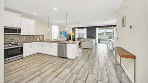 A spacious kitchen with white cabinets, a central island, and a dining area with a bench. - Modern Beautiful Private Pool Home! 9 Bedroom Villa (Davenport)