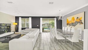 A modern living room with a sectional sofa, dining table with chairs, and a large abstract painting. - Modern Beautiful Private Pool Home! 9 Bedroom Villa (Davenport)