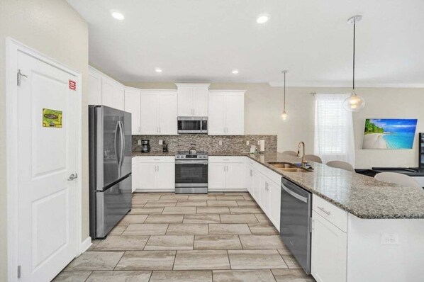 A modern kitchen with white cabinets, stainless steel appliances, and a granite countertop. - Modern Beautiful Private Pool Home! 9 Bedroom Villa (Davenport)