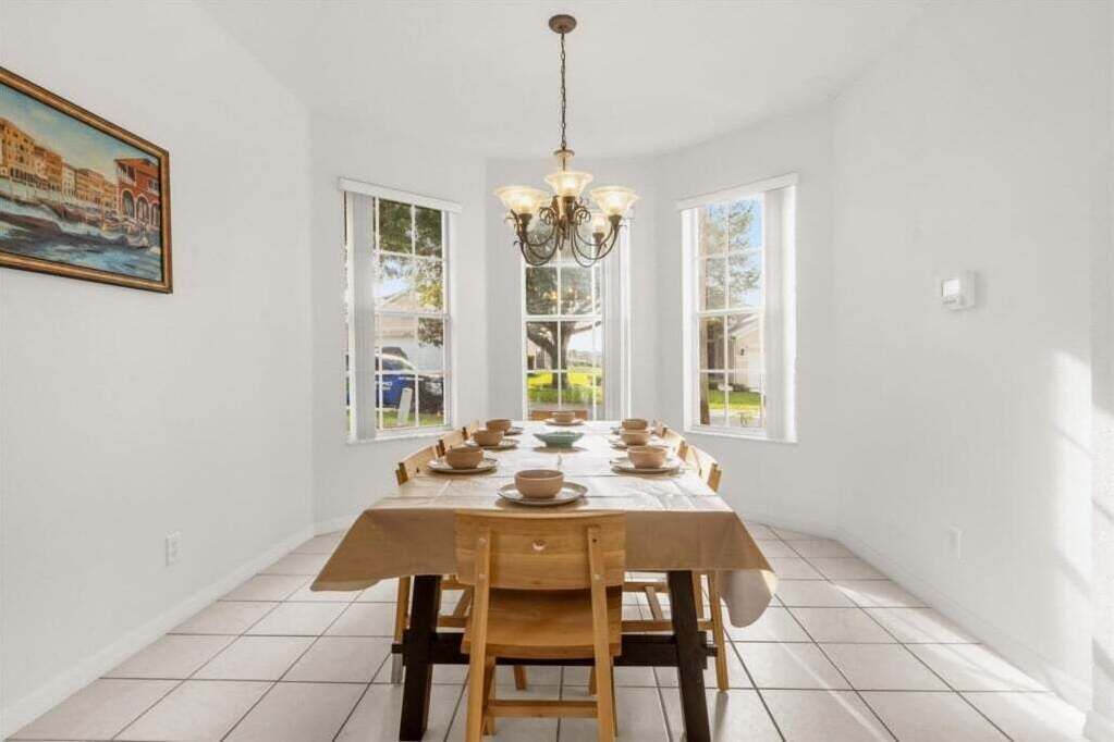 A dining room with a wooden table set for six, a chandelier, and a painting on the wall.