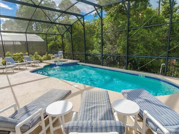 A covered outdoor swimming pool with lounge chairs and a table, surrounded by trees. - Southern Comfort Private Pool/spa Near Disney! 6 Bedroom Villa (Kissimmee)
