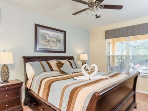 A bedroom with a bed, two bedside tables, a ceiling fan, a window with blinds, and a framed picture on the wall. - Southern Comfort Private Pool/spa Near Disney! 6 Bedroom Villa (Kissimmee)
