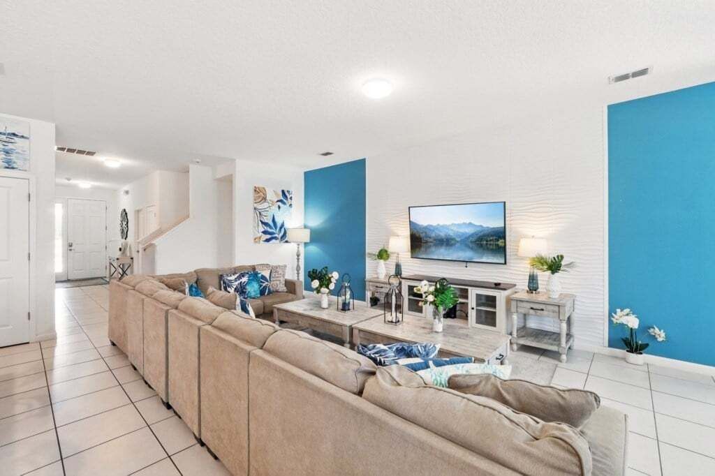 A modern living room with a beige sectional sofa, a flat-screen TV, and a blue accent wall.