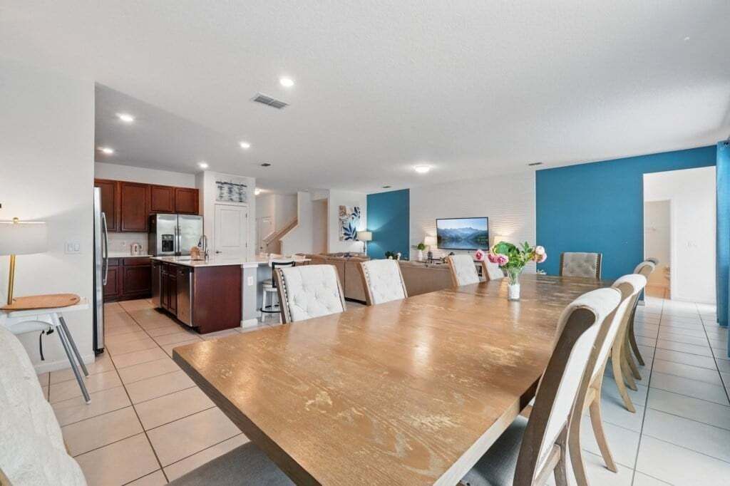 Un vaste espace de vie comprenant une grande table à manger en bois, une cuisine équipée d’appareils modernes et un mur d’accent bleu.