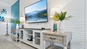 Een moderne woonkamer met een flatscreen televisie aan een gestructureerde muur, een witte consoles met tv-meubel, en decoratieve planten.