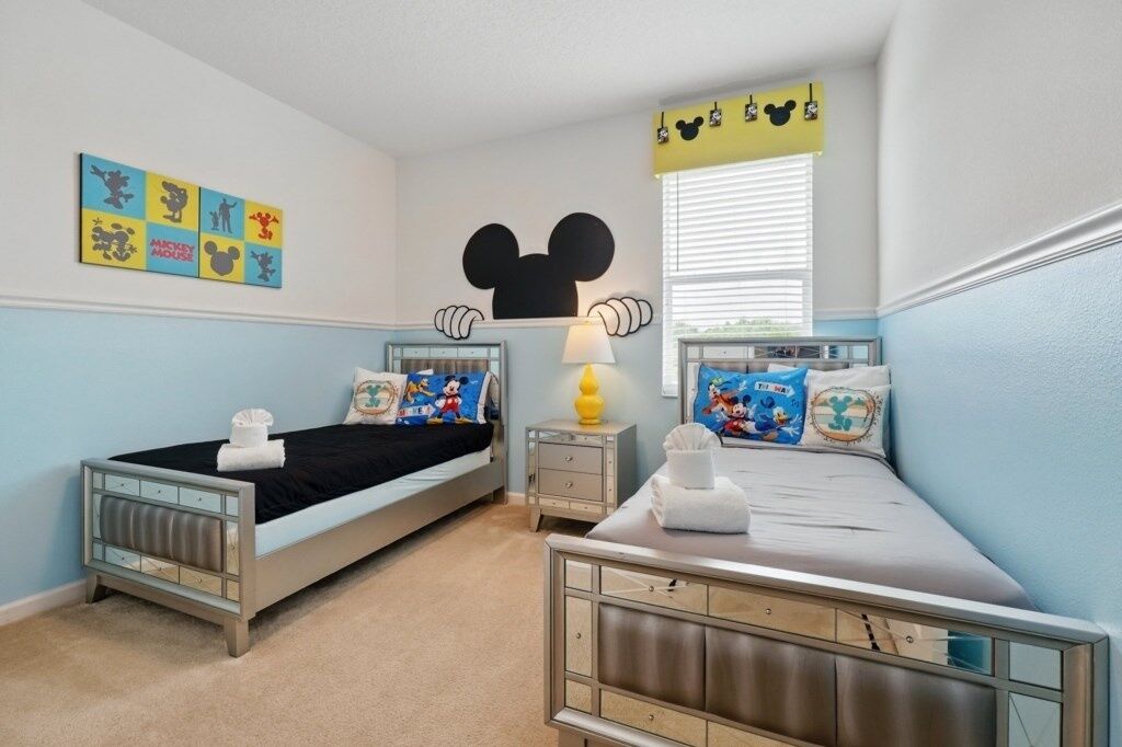 Habitación infantil con dos camas, decoración con la cabeza de Mickey Mouse y decoración de pared temática.