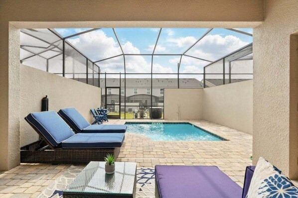Un espace piscine doté de chaises longues et d’un patio fermé par des baies vitrées.
