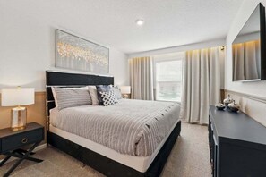 Quarto de hotel moderno com uma cama grande, mesa de cabeceira com luminária, cômoda e um espelho amplo.